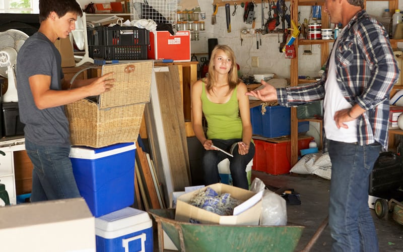 A father and his two teens work together to clean the garage.